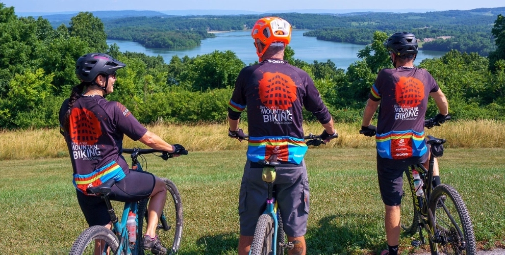 Three mountain bikers wearing a BAMBA jersey overlooking the Blue Marsh Lake